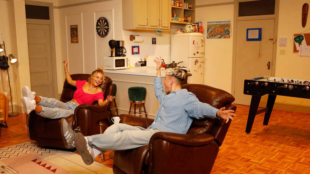 Two friends sit in Joey and Chandler's recliners at The Friends Experience.