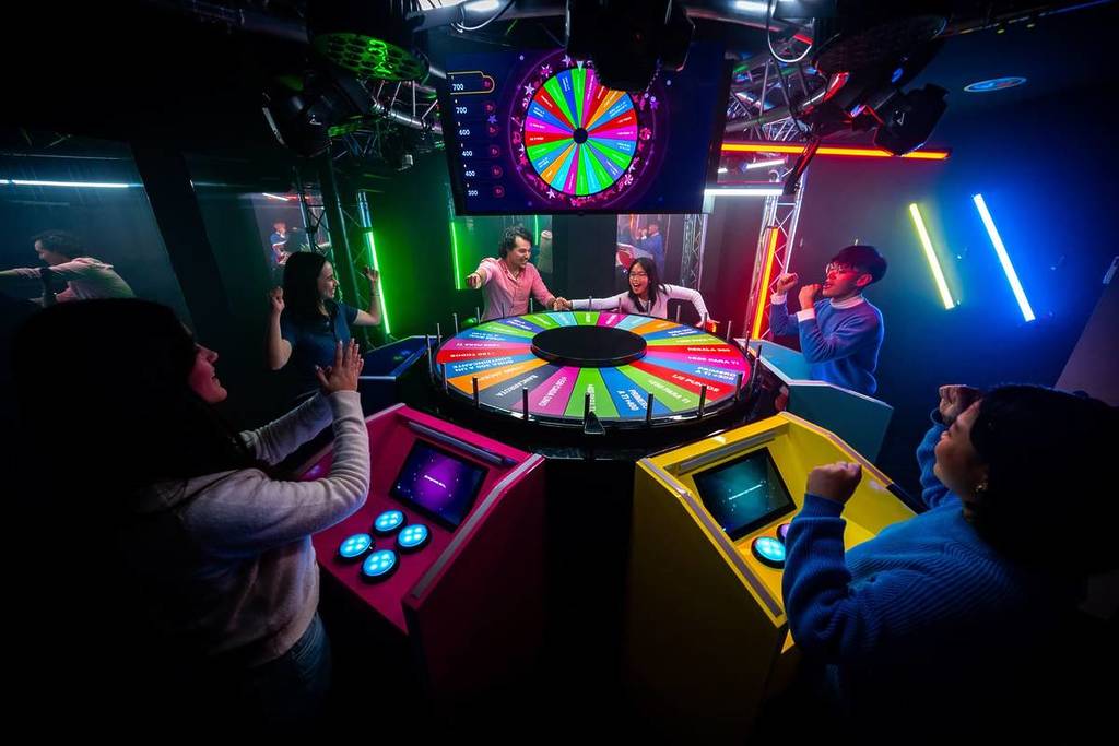 A wide shot of the room at BuzzAttack with the spinning wheel and colourful contestant podiums.