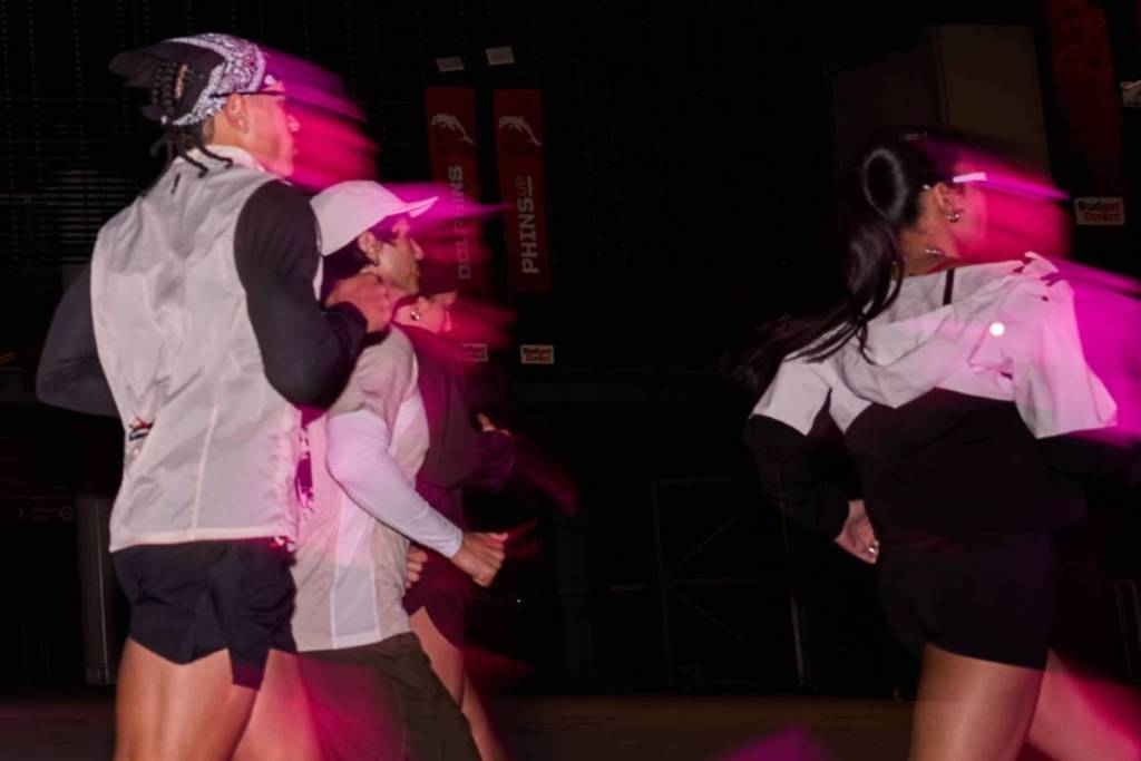 Runners move through a dark stadium illuminated by vivid pink lighting, creating a dynamic motion-blur effect