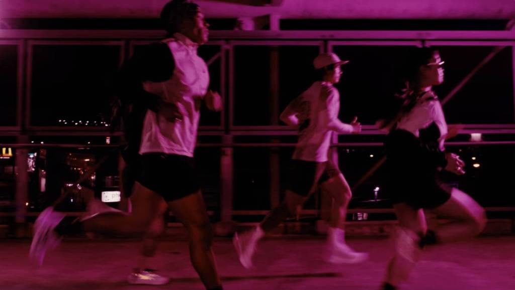 three runners in a neon pink illuminated run through suncorp stadium in brisbane