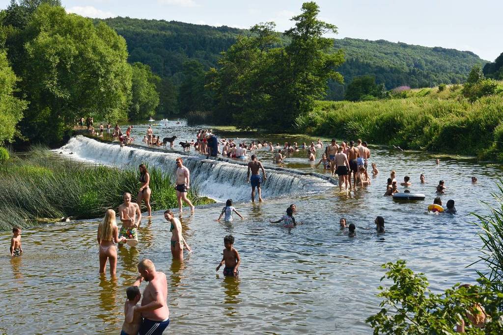People walking across and swimming and enjoying the good weather in River Avon on a busy day. Warleigh Weir, offering outdoor swimming near Bristol