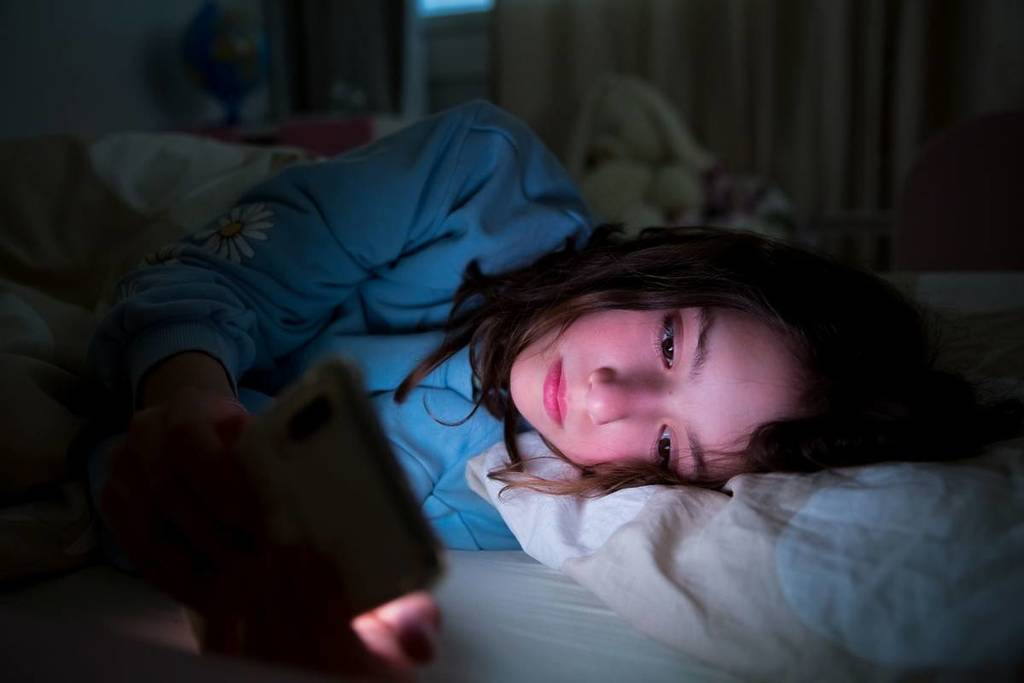 A child using smart phone lying in bed late at night, playing games, watching videos online, scrolling screen. Children's screen addiction. Child's room at night.