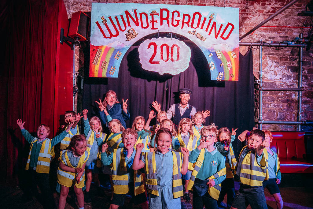 Schoolchildren and Invisible Circus members in front of a Wunderground 200 sign