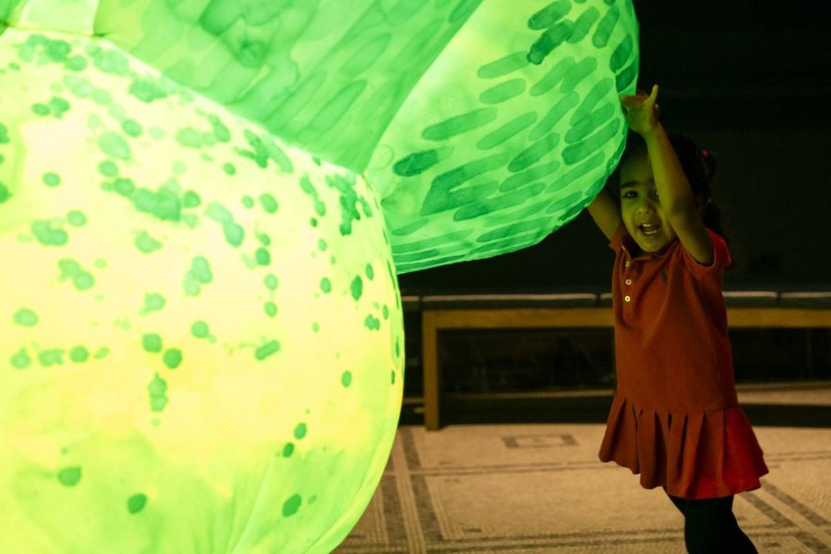 A young child cuddling a large inflatable lit up plant.