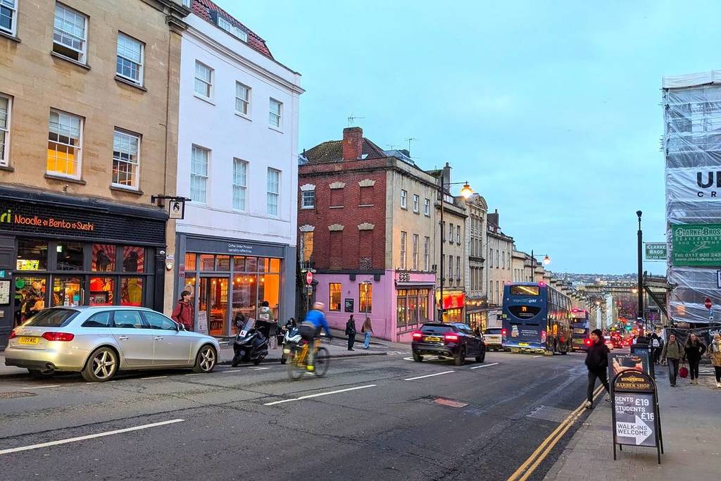 : Evening scene of people and traffic on the lively Park Street lined with historic buildings and shops under a twilight sky