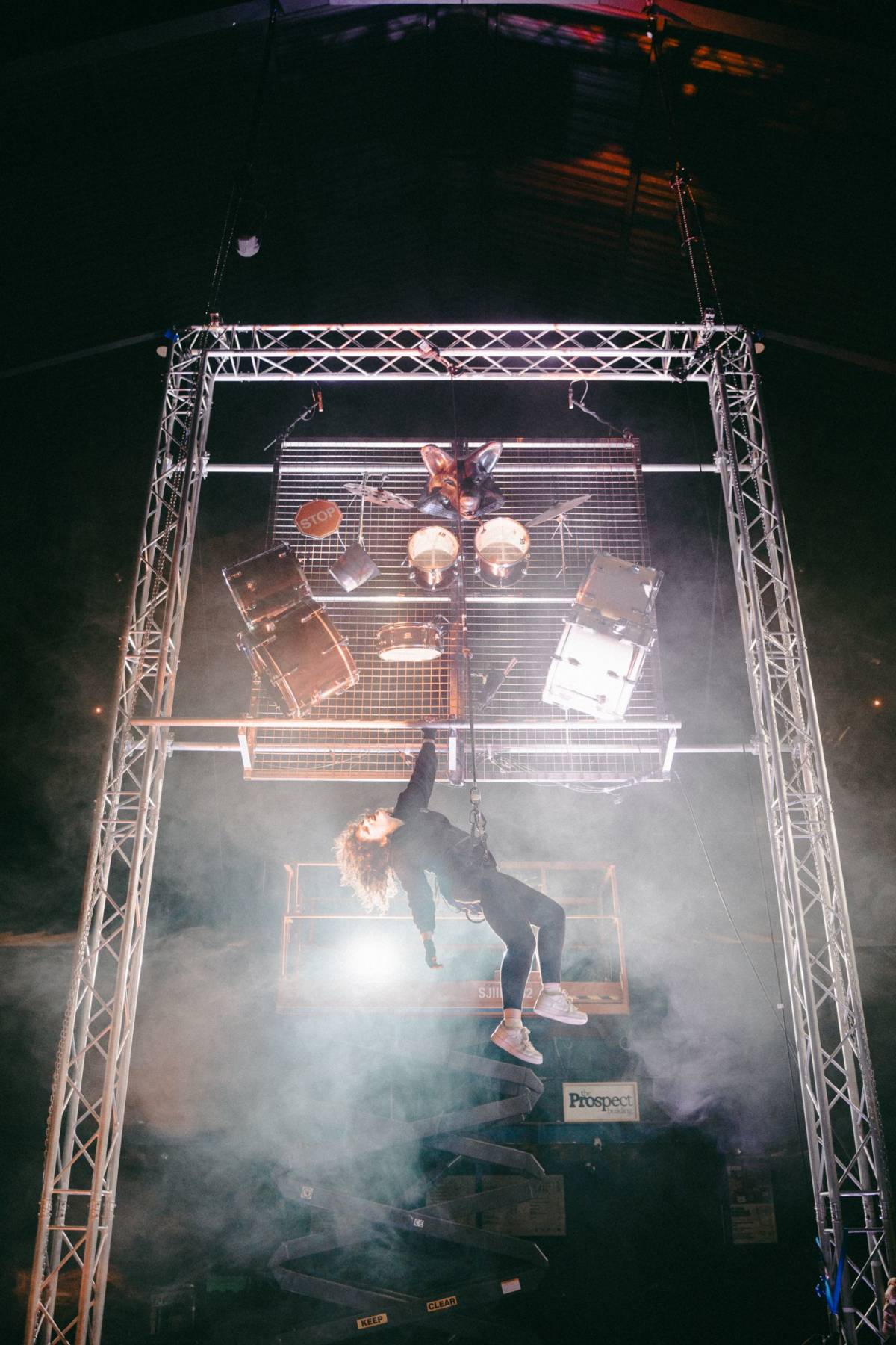 Invisible Circus performer dangling below a mounted drum kit