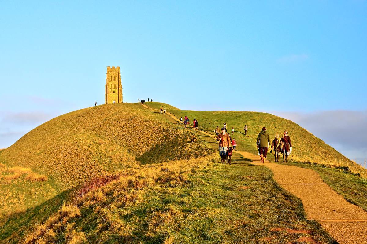 Glastonbury, UK - December 30, 2019: Tourists visiting Glastonbury Tor, in a golden winter sunset with clear blue skies