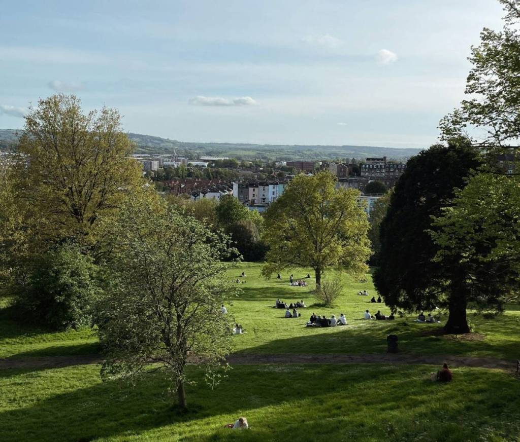 a park in bristol with groups of people sitting on the grass