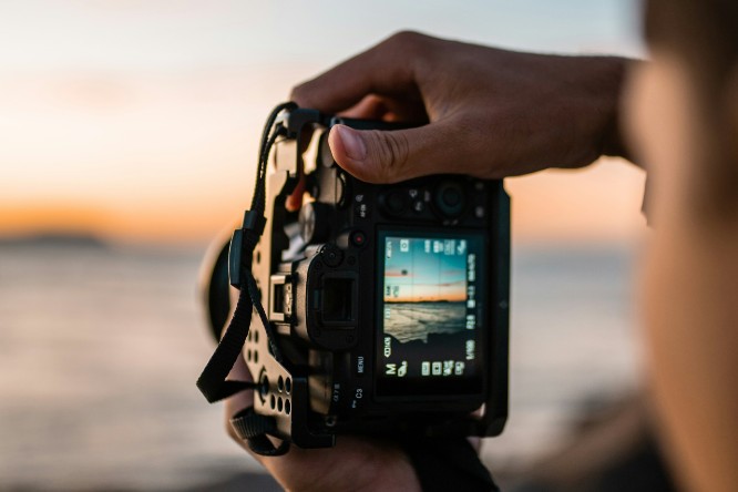 a person holds up a camera looking through the viewfinder at a seascape