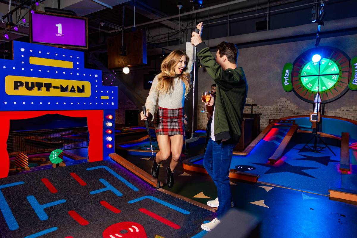 A couple enjoying a round of tech-infused mini golf at Puttshack, smiling and holding putters on a neon-lit course