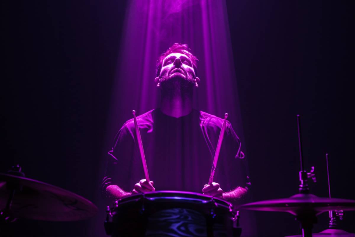A drummer looking up while playing the drums under purple lighting at We call it Drums
