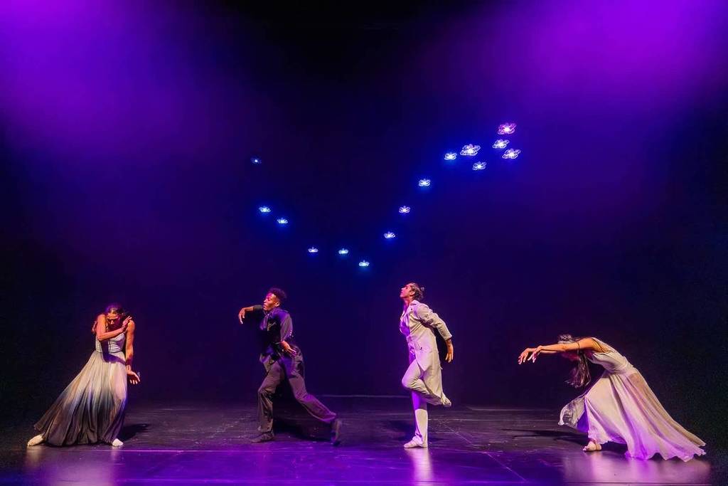 four performers dance on stage under drone lights