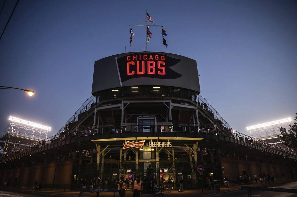 As dusk falls over Wrigley Field, stadium lights glow against the deepening sky, casting a golden hue over the field. Fans settle in for the evening as the iconic scoreboard lights up and the city skyline begins to twinkle in the distance.