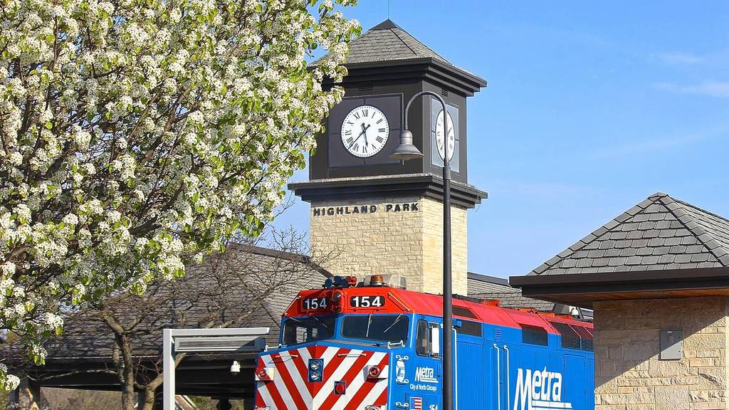 A late springtime late afternoon view of a Metra train stopped at the Highland Park station, with clock tower and white tree blossoms.
