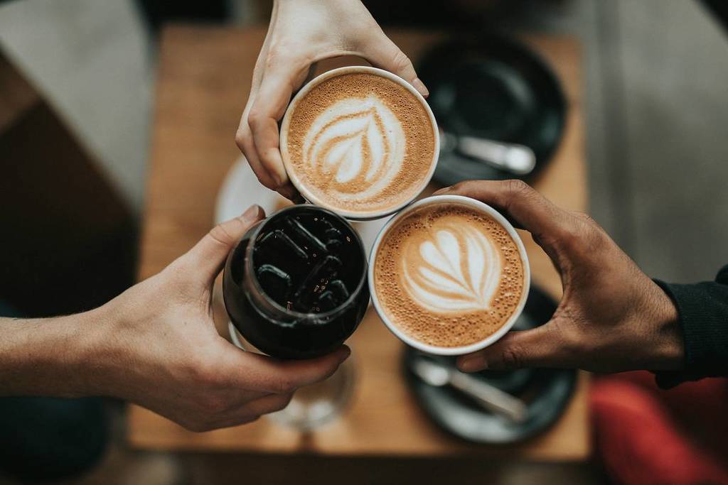 Three people hold cups of coffee at a cafe.