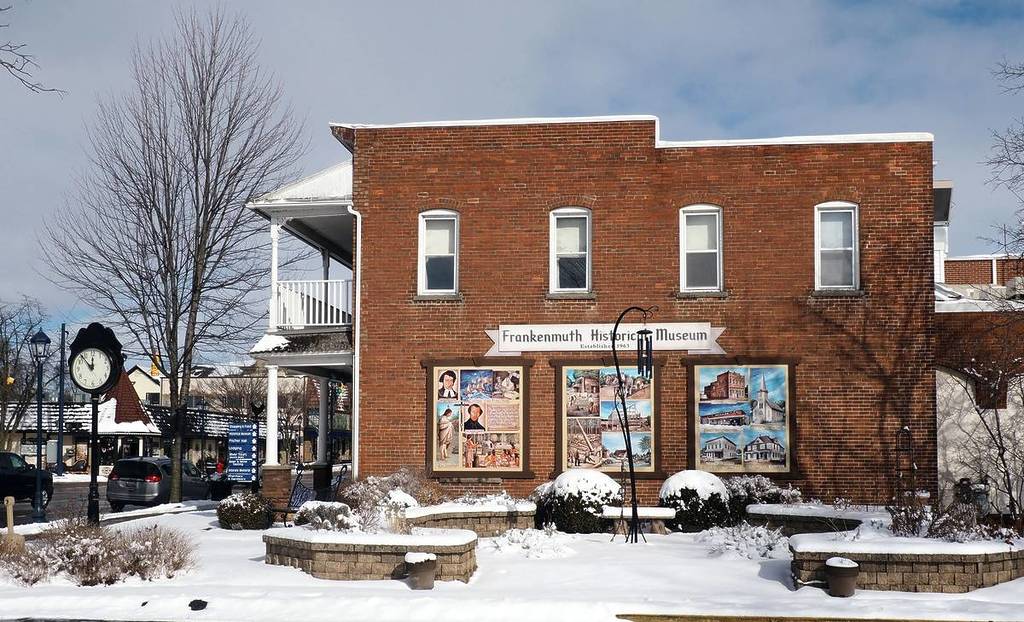 central part with Main street on the left and Frankenmuth Historical Museum in front (brick wall with graffiti). Winter day with snow, no people.
