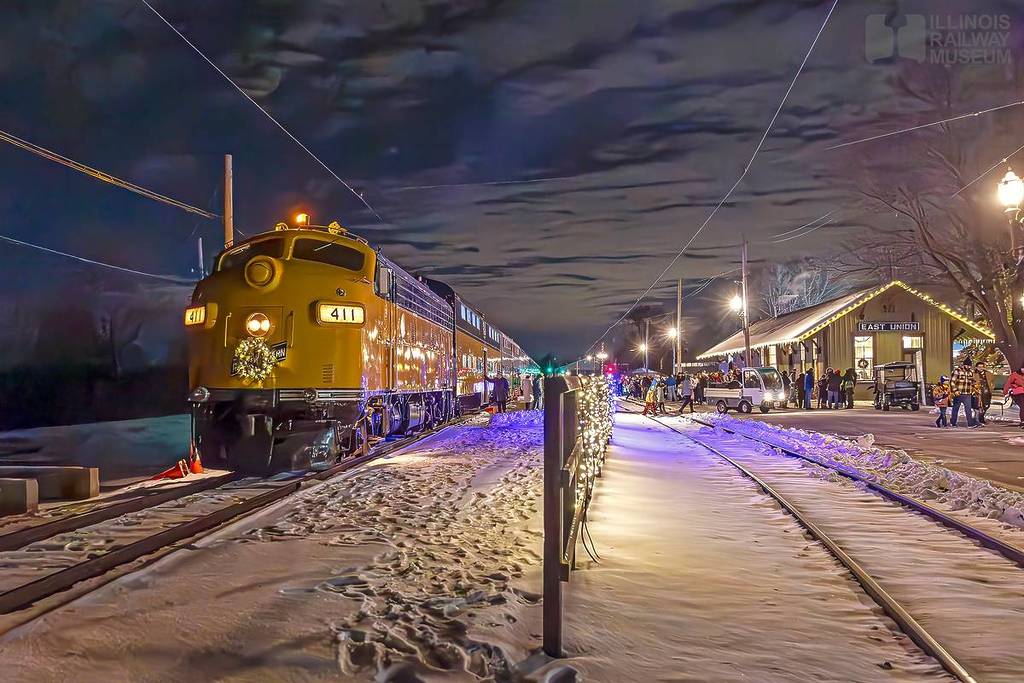 A train in the snow surrounded by holiday lights.