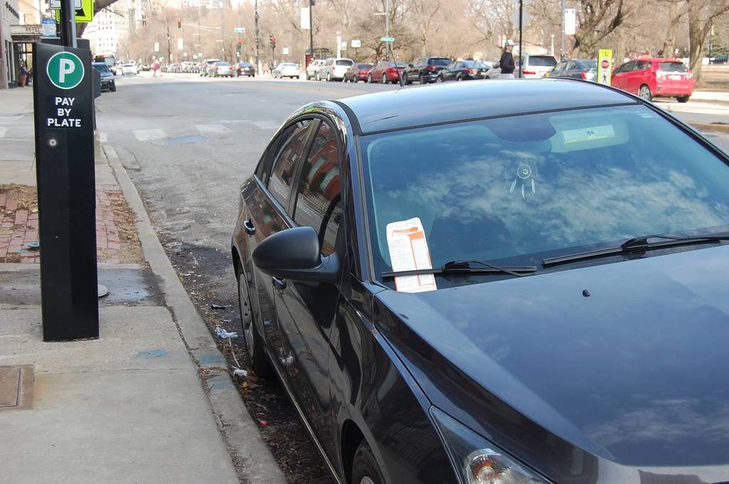 un coche negro aparcado ilegalmente a pocos metros del parquímetro recibe una multa por infringir la ordenanza de la ciudad de Chicago.