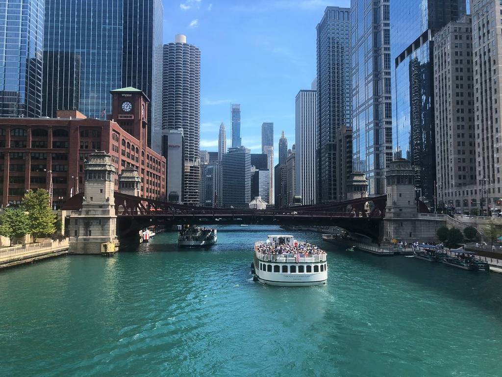 A boat sails across the Chicago River, surrounded by skyscrapers.