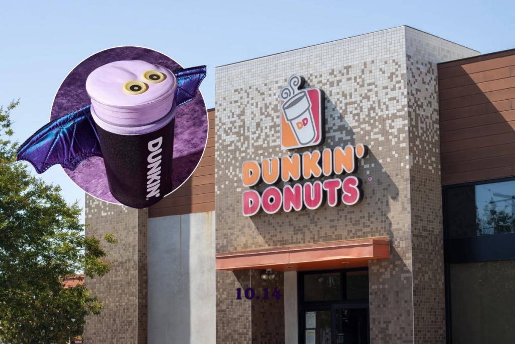 Free Dunkin bat koozie with purple wings on a Berry Battie Daydream Refresher topped with purple cold foam and edible eyes, in front of a Dunkin' Donuts storefront