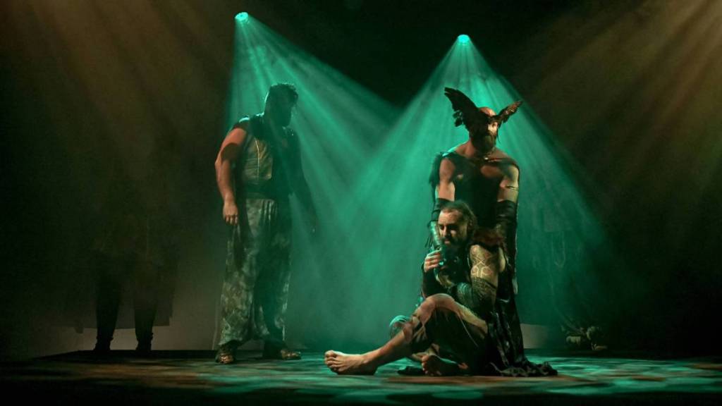 Hombres actuando en el escenario bajo una dramática iluminación verde durante Mythos: Ragnarök