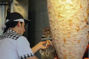 A man trims a chicken kebab at a Greek restaurant. 