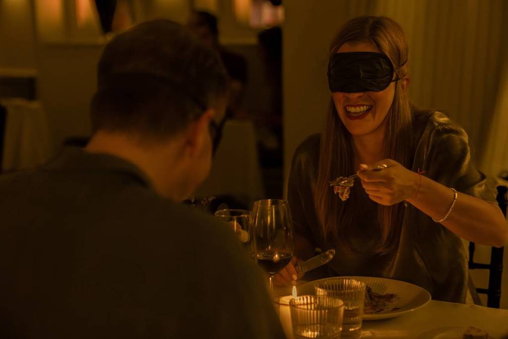 A blindfolded couple enjoying dinner at an elegant restaurant