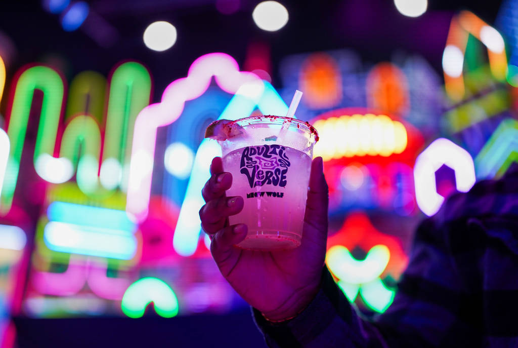 Image shows someone holding a colorful cocktail with blurring neon lights in the background at Meow Wolf Grapevine.