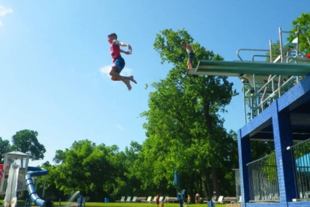 Image shows a kid jumping off a diving board at Burgers Lake in Fort Worth.