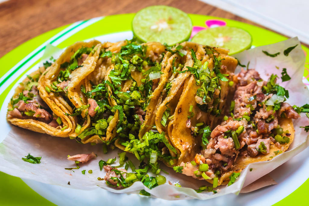 Image shows a tray of tacos with two limes in the background.