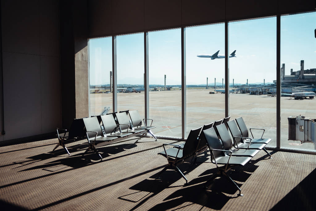 Image shows the waiting area of an airport with a plane taking off in the background.