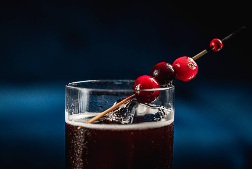 La imagen muestra la guarnición de arándanos de un cóctel oscuro elaborado por Apothecary en Dallas.