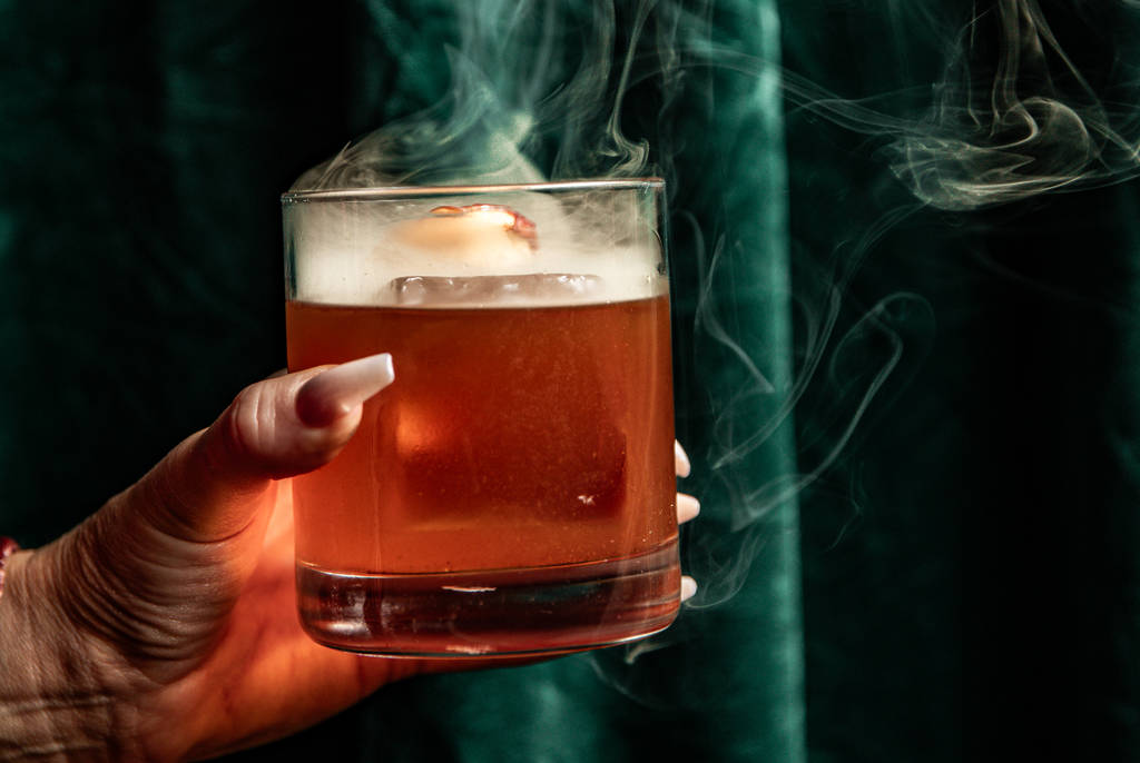 Image shows a cocktail with wisps of smoke coming off the top as made by Apothecary in Dallas.
