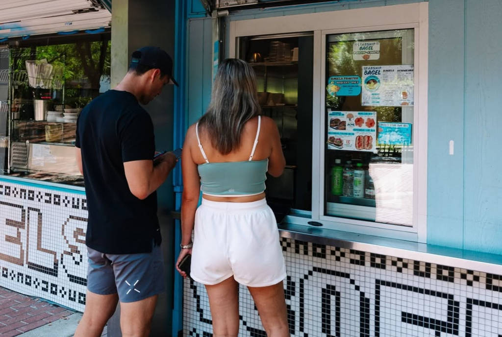Image shows two customers visiting the window at Starship Bagel in Dallas, Texas.
