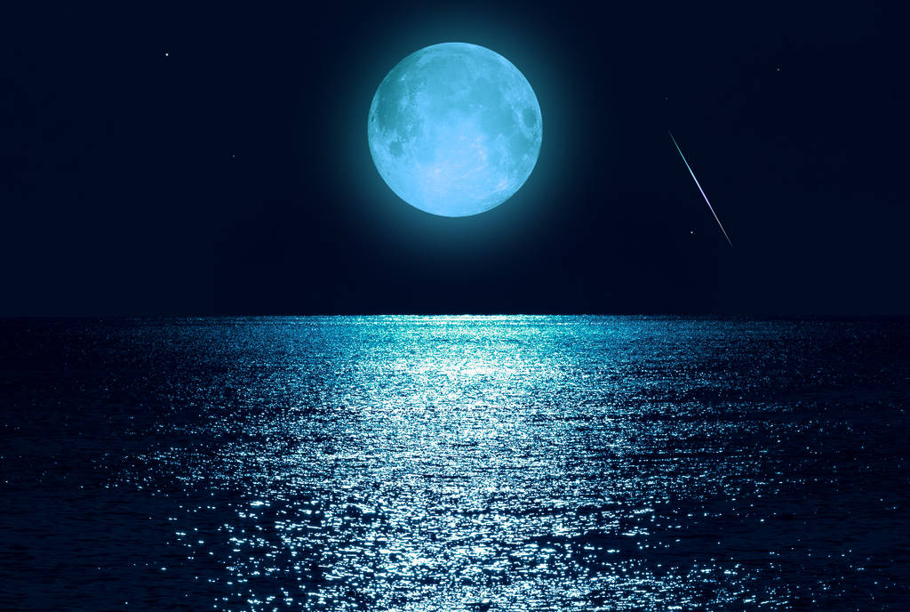 Image shows a blue-tinted supermoon above a body of water.