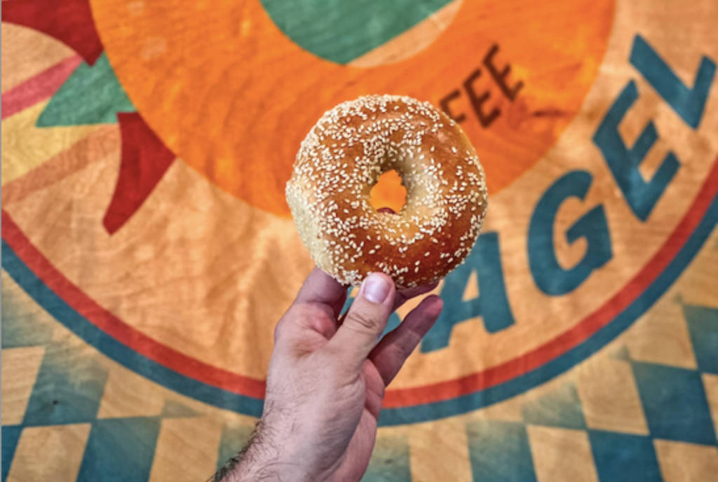 Image shows someone holding up a bagel in front of the Starship Bagels sign.