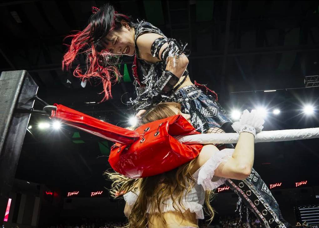 Image shows a TJPW pro wrestler in mid-air as she leaps into an opponent in the corner of the ring.
