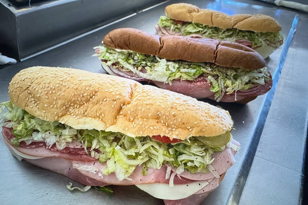 Image shows three sandwiches of DIno's Subs displayed on a countertop.