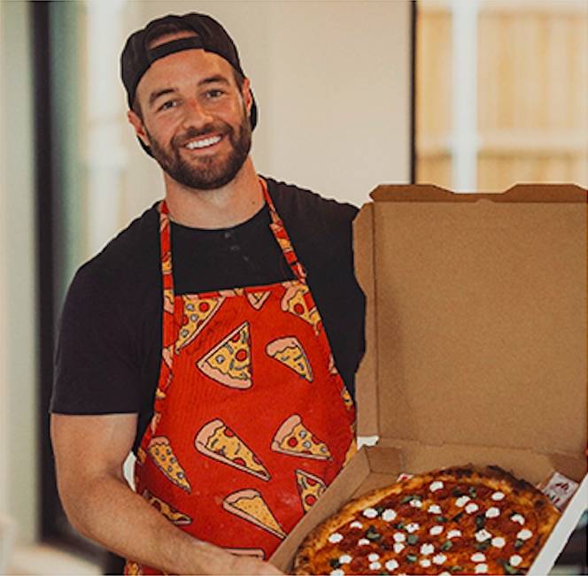Image shows Dave of Dave's Pizza Oven posing with a pizza in a box and an apron.