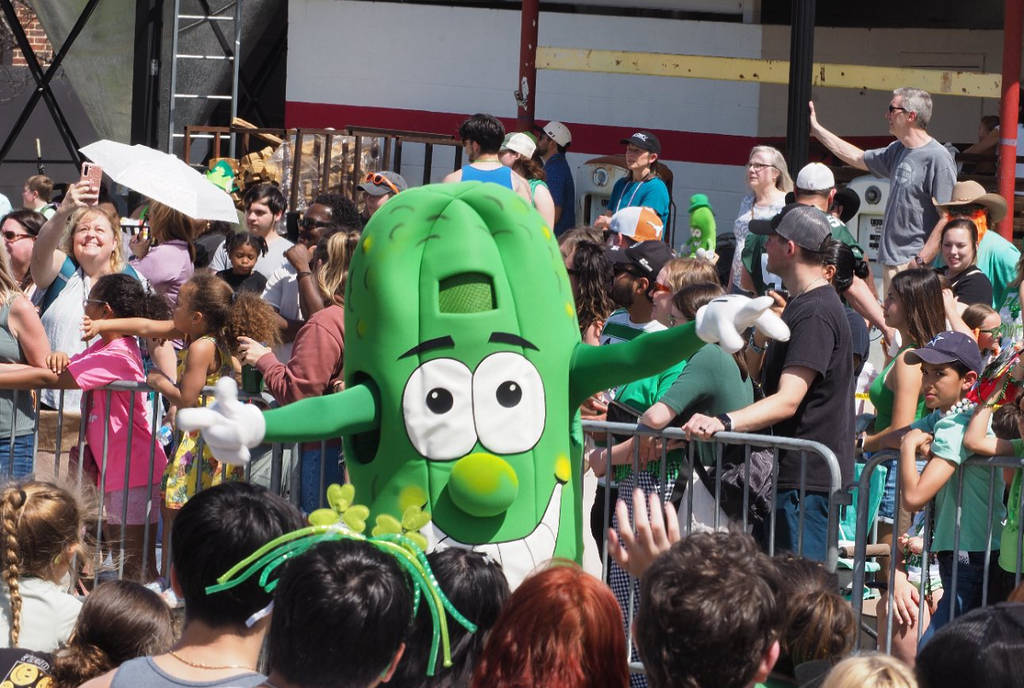 Image shows someone in a pickle costume dancing among a crowd of people.