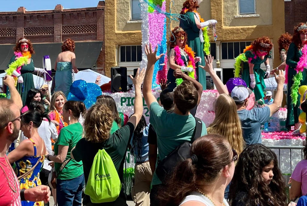 Image shows a float in the Mansield Pickle Parade surrounded by a crowd of people.