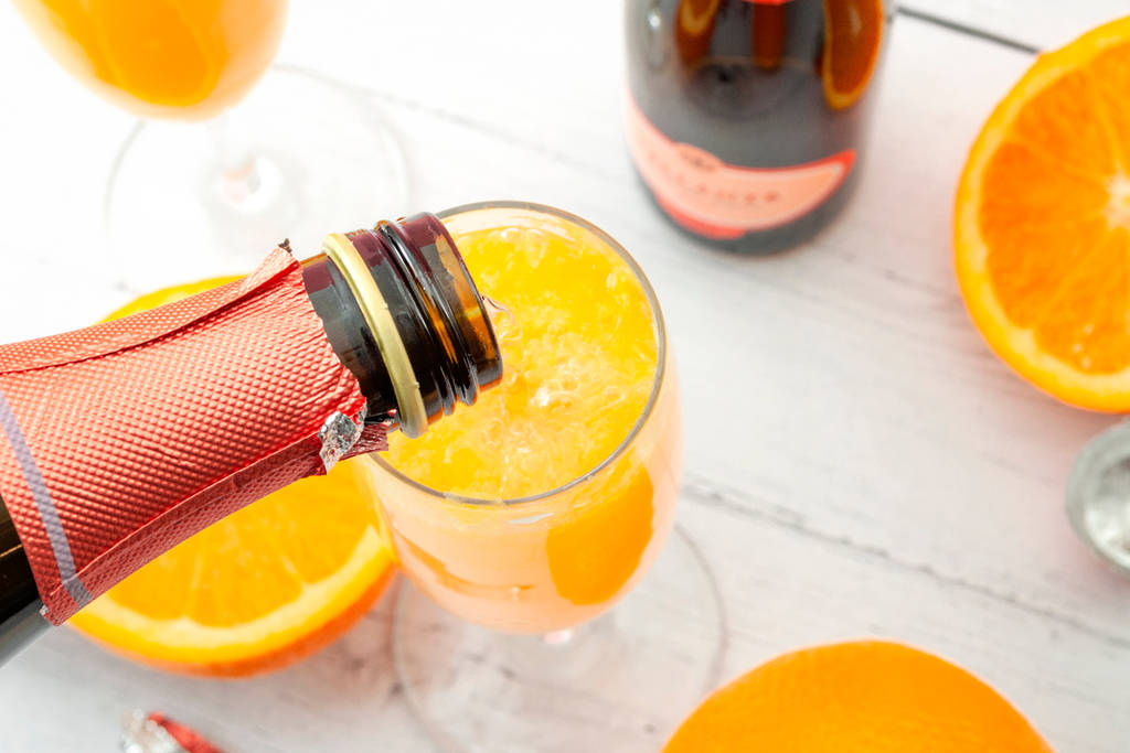 Image shows a bottle of champagne being poured into a glass of mimosa.