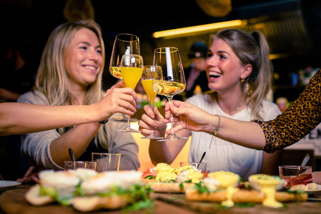 Image shows a group of women clinking glasses of mimosas at brunch. 