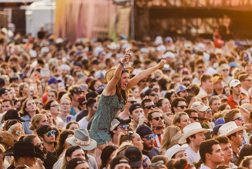 Image shows a woman raising her hands in the crowd at a festival.