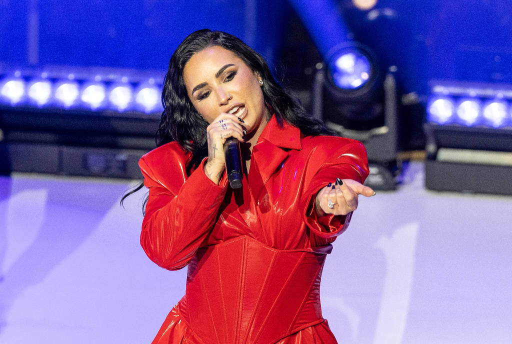 Image shows Demi Lovato performing on stage while wearing a red suit.