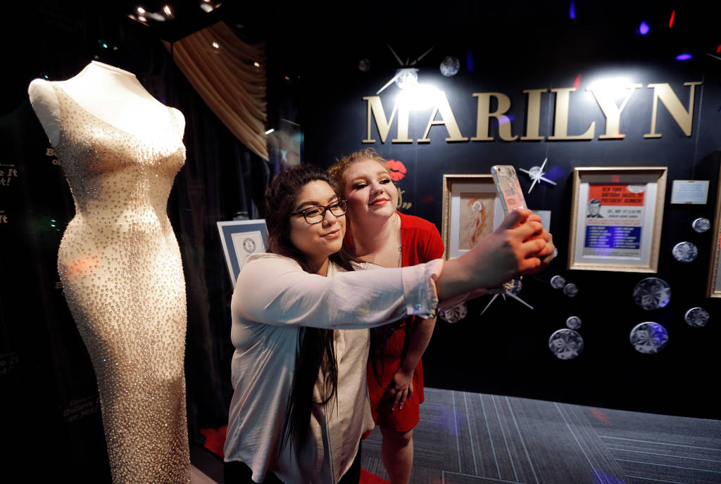 La imagen muestra a dos chicas haciéndose una foto delante del vestido de Marilyn Monroe.