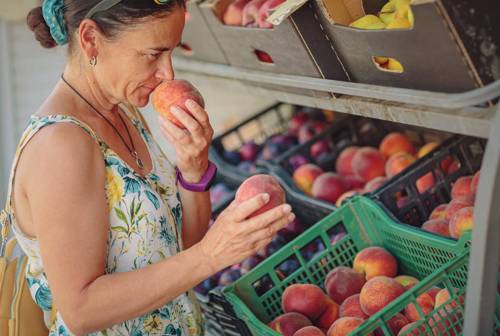 Image shows a woman smelling a peach.