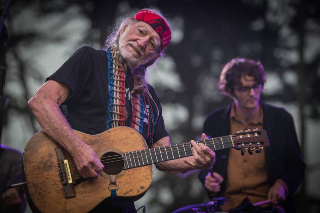 La imagen muestra a Willie Nelson tocando la guitarra en el escenario.