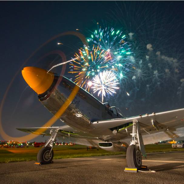 La imagen muestra un avión con fuegos artificiales de fondo en el Addison Kaboom Town!