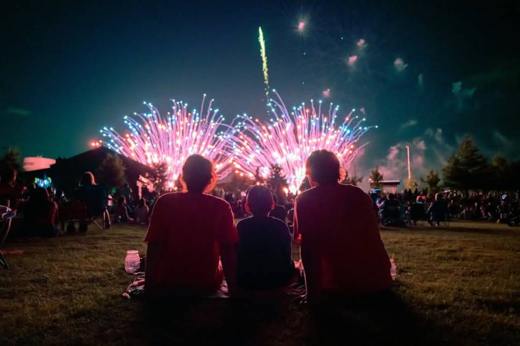 La imagen muestra a una pequeña familia contemplando un espectáculo de fuegos artificiales en el «Red, White, and BOOM!» de McKinney.